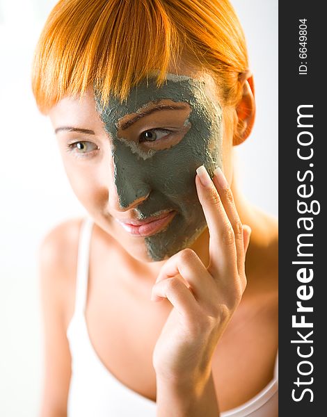 Young red-haired woman put green mask on half face. She's smiling and looking at camera. Closeup on face. Young red-haired woman put green mask on half face. She's smiling and looking at camera. Closeup on face.
