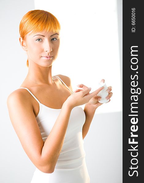 Young red-haired woman applying cream. She's looking at camera.