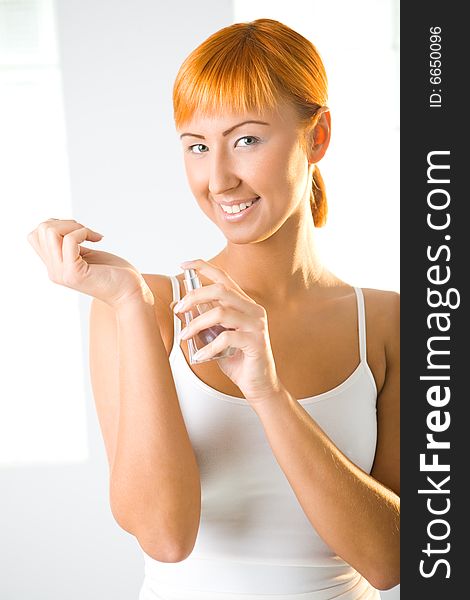 Young woman holding a bottle of perfume. She's smiling and looking at camera. Front view. Young woman holding a bottle of perfume. She's smiling and looking at camera. Front view.