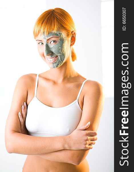 Young red-haired woman with green mask on half face. She's standing with crossed hands and smiling. Looking at camera. Young red-haired woman with green mask on half face. She's standing with crossed hands and smiling. Looking at camera.