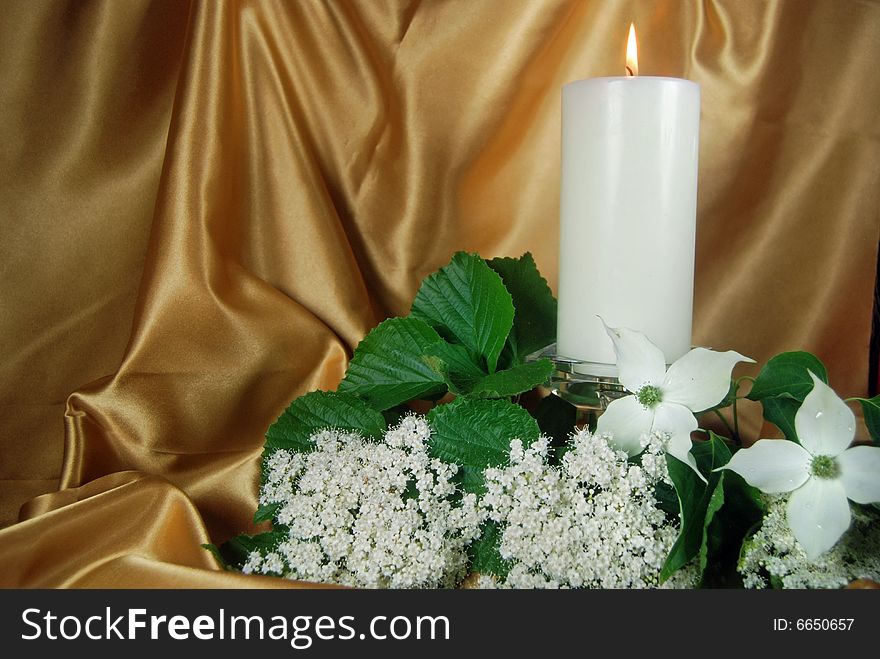 Glowing candle and dogwood on gold satin. Glowing candle and dogwood on gold satin.