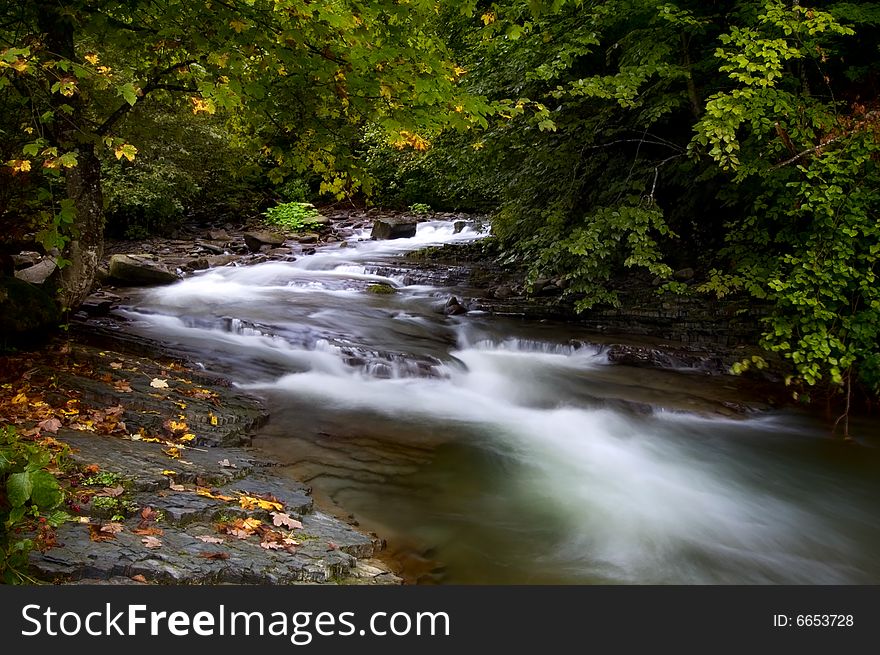 Little cascade of waterfalls in a peaceful wood. Green background and the dark rocks contrast. Waterfall motion blur. Little cascade of waterfalls in a peaceful wood. Green background and the dark rocks contrast. Waterfall motion blur.