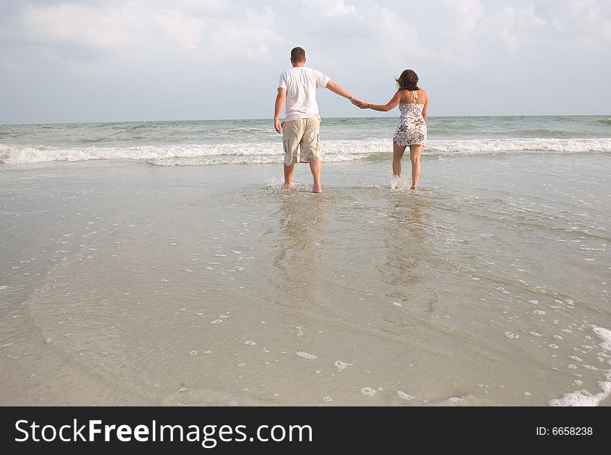 Couple walking at the beach holding hands in the ocean