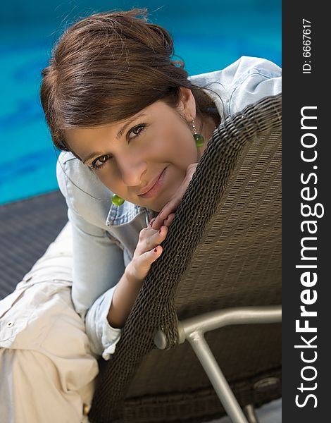 Pretty girl is sitting on the trestle-bed near a pool. Pretty girl is sitting on the trestle-bed near a pool