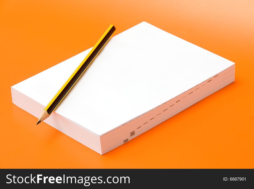 Blank book and pencil over an orange background
