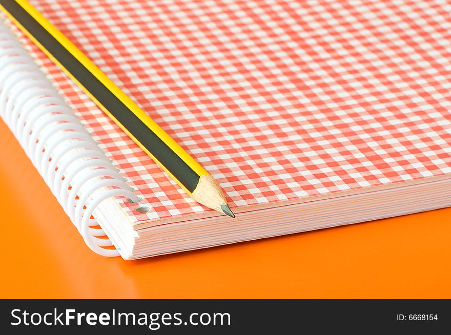 Pencil and notebook over an orange background. Pencil and notebook over an orange background