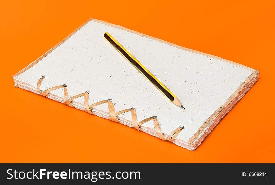 Recycled notepad and pencil over an orange background. Recycled notepad and pencil over an orange background