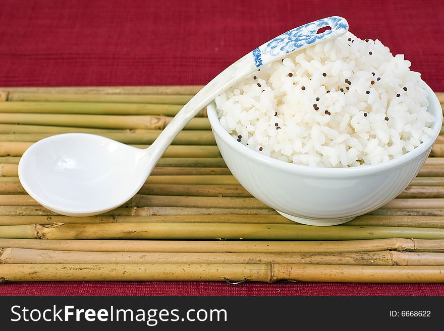 White bowl of boil chinese rice with soup spoon over bamboo