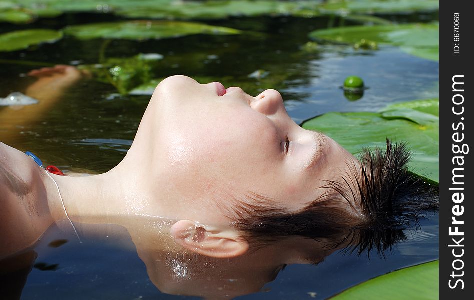 The portrait of a boy laying down in a lake with closed eyes. The portrait of a boy laying down in a lake with closed eyes.