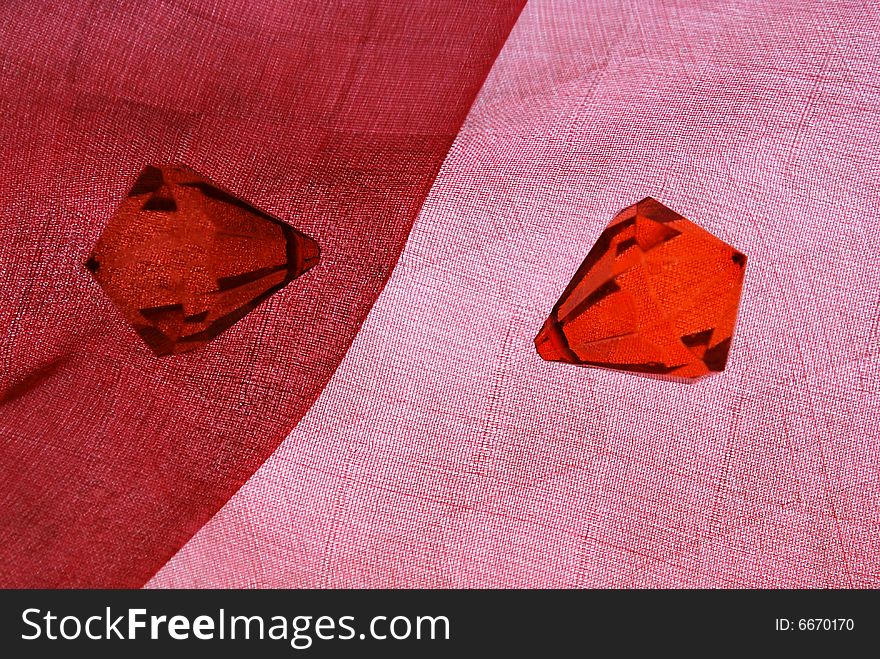 Two red plastic diamonds on fabric. Two red plastic diamonds on fabric