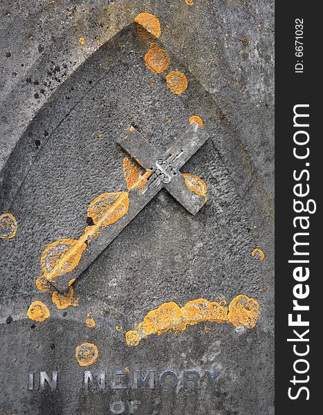 Old gravestone covered in lichens with a carved stone cross and the words in memory of.