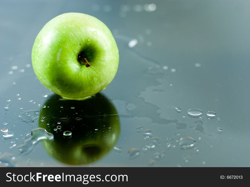 An apple reflecting on a glass surface with water drops around it