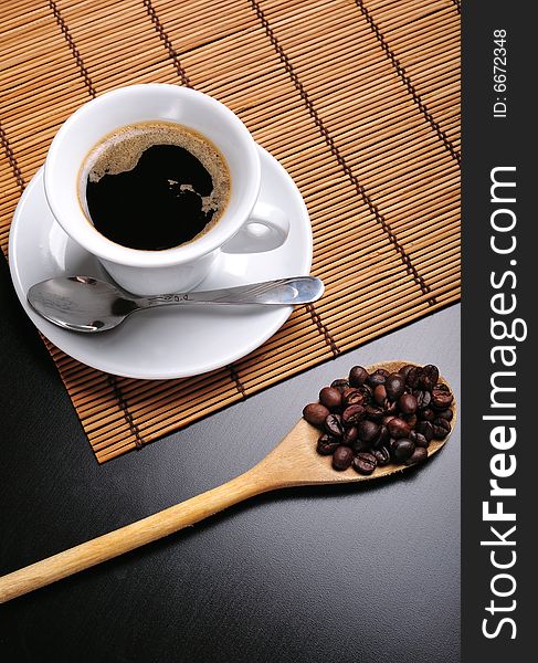 Close up of a white cup of coffee and a wooden spoon with beans. Close up of a white cup of coffee and a wooden spoon with beans