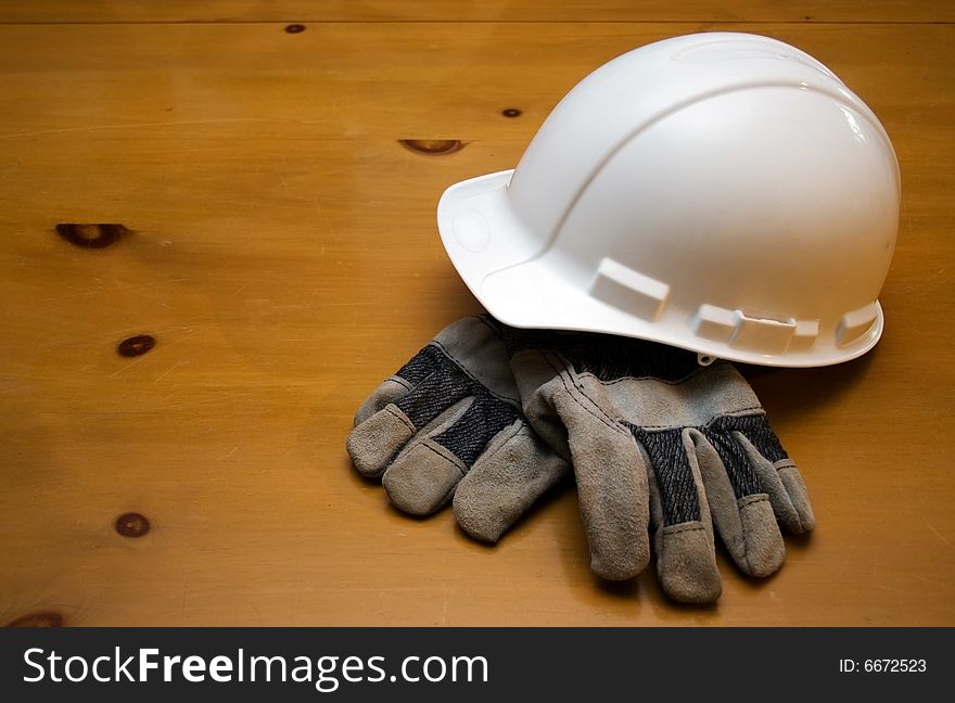 White hard hat and gloves resting on a wood surface. White hard hat and gloves resting on a wood surface