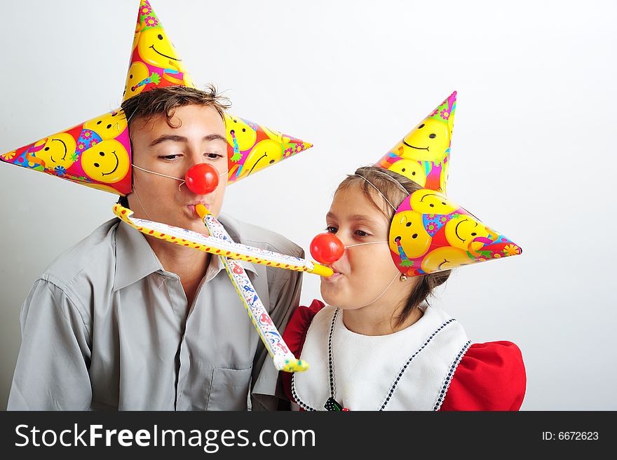 A little girl and a boy with party horn and clown noses