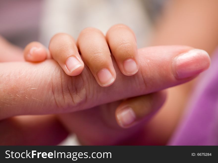 Tiny newborn baby fingers wrapped around adult female fingers up close. Tiny newborn baby fingers wrapped around adult female fingers up close