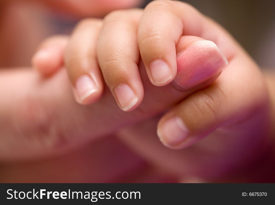 Tiny newborn baby fingers wrapped around adult female fingers up close. Tiny newborn baby fingers wrapped around adult female fingers up close