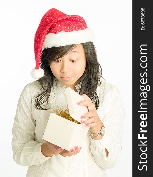 Teenager girl with Santa Claus hat peeking as she opens a gift in a cube box filled with golden straw. Teenager girl with Santa Claus hat peeking as she opens a gift in a cube box filled with golden straw