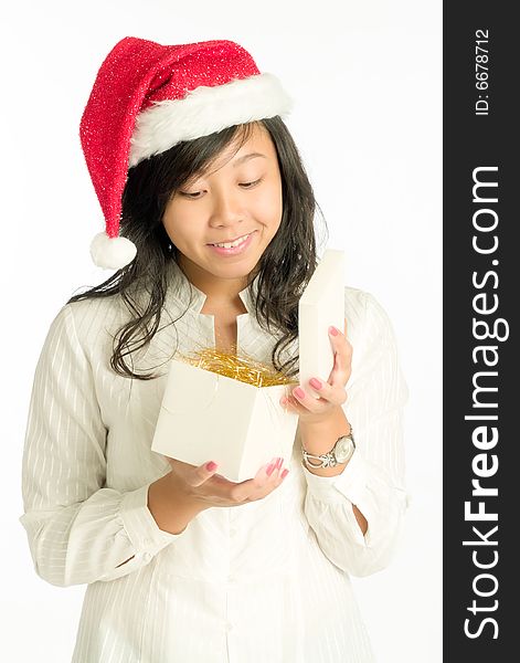 Teenager girl with Santa Claus hat opening a gift in a cube box filled with golden straw. Teenager girl with Santa Claus hat opening a gift in a cube box filled with golden straw