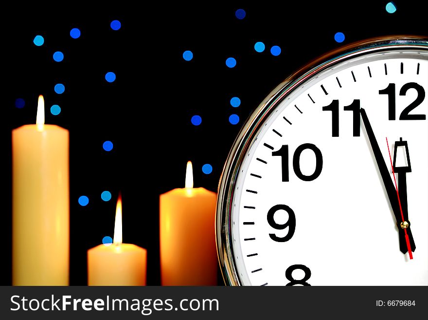 Clock set at three minutes to midnight with blue Christmas lights in background and candles burning