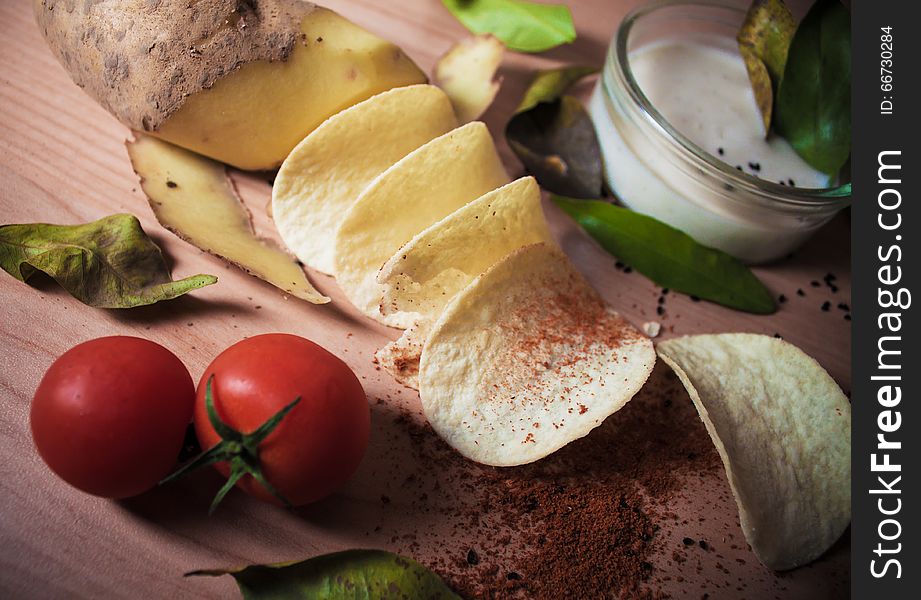 Potato chip manufacturing process. Potatoes, chips, tomatoes, sauce, spices, bay leaves, cumin, paprika on a wooden background. Potato chip manufacturing process. Potatoes, chips, tomatoes, sauce, spices, bay leaves, cumin, paprika on a wooden background.