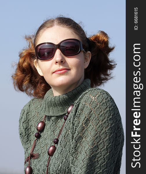 Old-fashioned Young curly girl in a vintage gray knitted dress in sunglasses. Blue background. Girl in sunglasses is looking at someone