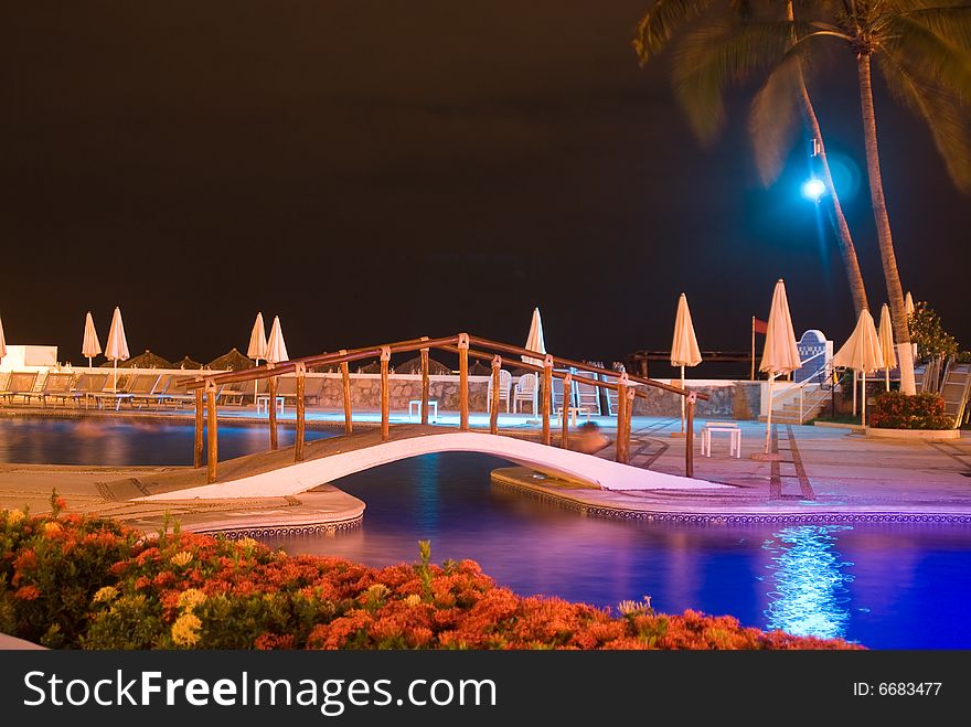 Swimming pool at night lit by a dramatic and interesting light with shades of blue, orange, green, purple and tan colors. Swimming pool at night lit by a dramatic and interesting light with shades of blue, orange, green, purple and tan colors