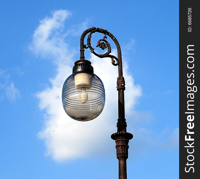 Three ornate street lamps on a lamp post against a blue sky in Romania