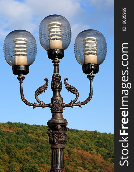 Three ornate street lamps on a lamp post against a blue sky in Romania