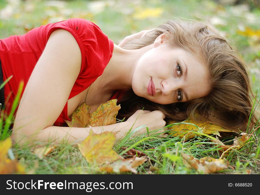 Beautiful young woman lying on the grass with yellow leaves. Beautiful young woman lying on the grass with yellow leaves