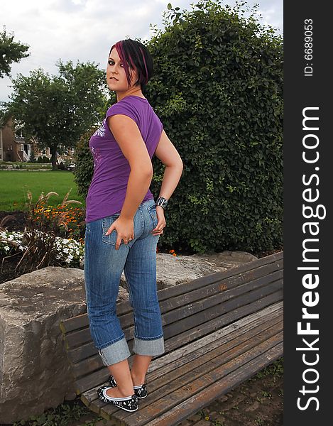 An red hair girl in jeans standing on a park bench on lake Ontario at sunset. An red hair girl in jeans standing on a park bench on lake Ontario at sunset.