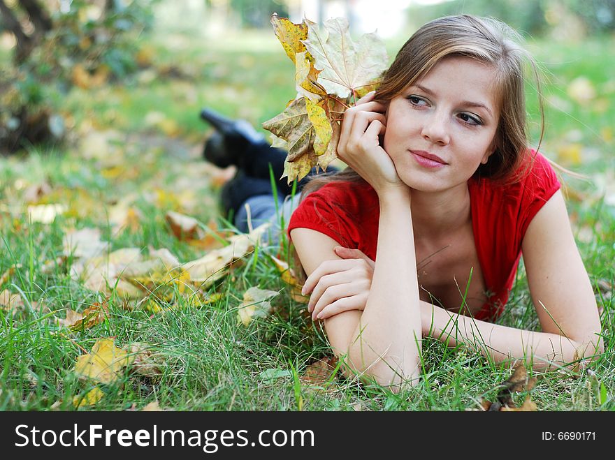 Young beautiful woman lying on the green grass with maple leaf. Young beautiful woman lying on the green grass with maple leaf