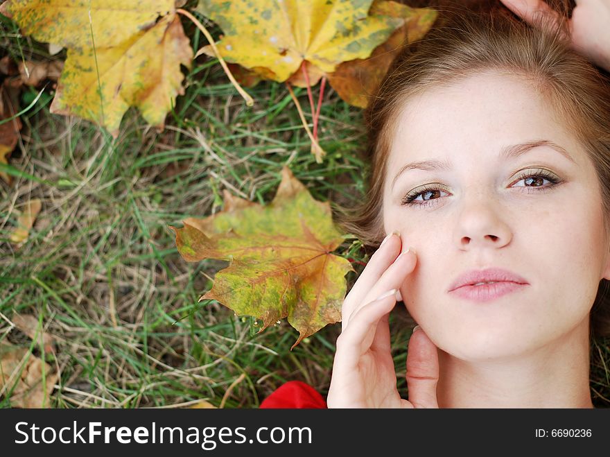 Young beautiful woman lying on the green grass with maple leaf. Young beautiful woman lying on the green grass with maple leaf