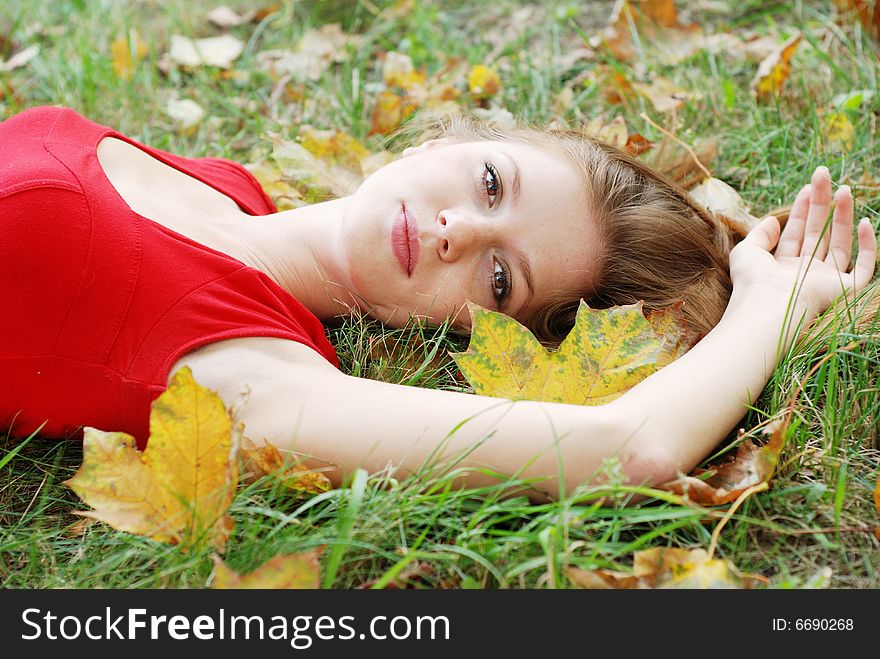 Beautiful young woman lying on the grass with yellow leaves. Beautiful young woman lying on the grass with yellow leaves