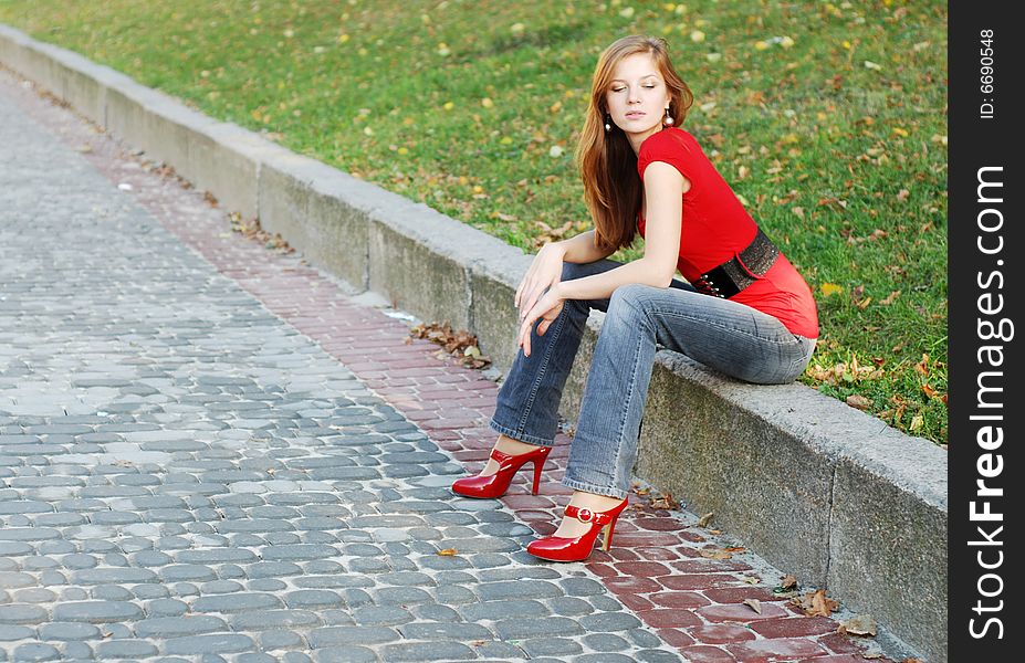 Beautiful woman sit on a road kerb in park. Beautiful woman sit on a road kerb in park