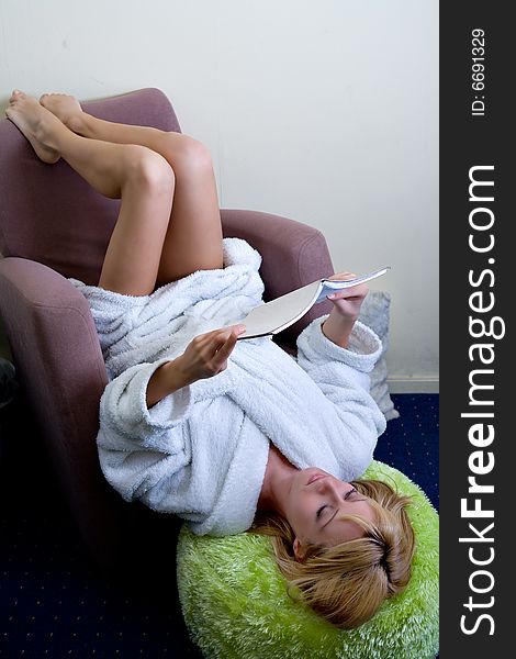 Blond model  is reading a book while laying upside down in her chair. Blond model  is reading a book while laying upside down in her chair