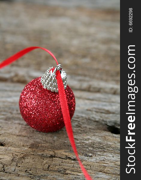 A red Christmas ornament with a red ribbon on an old piece of wood for a rustic look.  A soft focus effect to add a bit of elegance also copy space available.