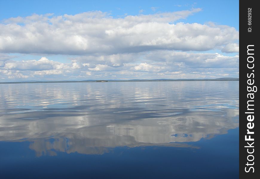 Bright blue sky and reflection of it and the clouds in clear lake water. Bright blue sky and reflection of it and the clouds in clear lake water