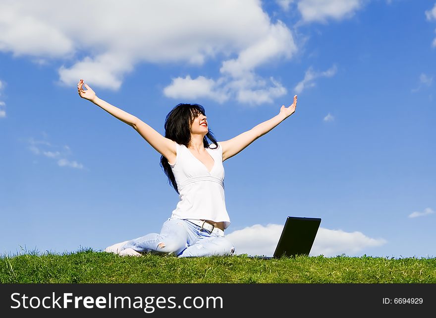 Pretty woman with laptop on the green grass