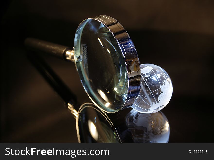 Close-up of magnifier and little glassy earth on dark background. Close-up of magnifier and little glassy earth on dark background