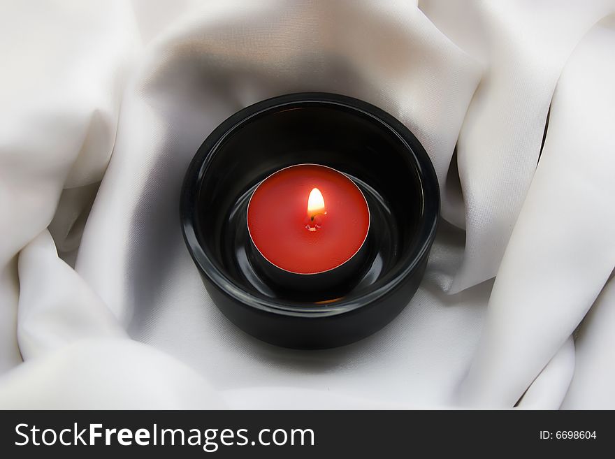 Candle in candlesticks on white silk