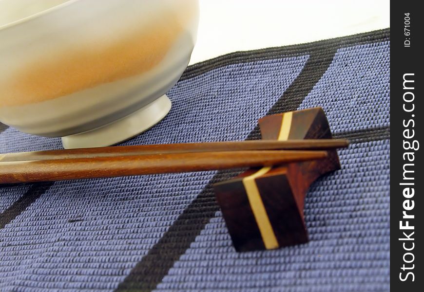 Perspective with chopsticks and bowl on a textile blue mat.Soft focus on the pointed end of the chopsticks,main focus in the middle of the image. Perspective with chopsticks and bowl on a textile blue mat.Soft focus on the pointed end of the chopsticks,main focus in the middle of the image.