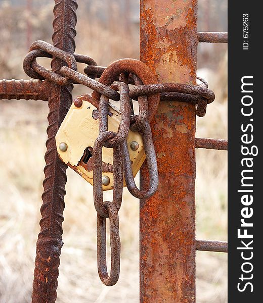 A rusty padlock attached to a metal gate and chain.