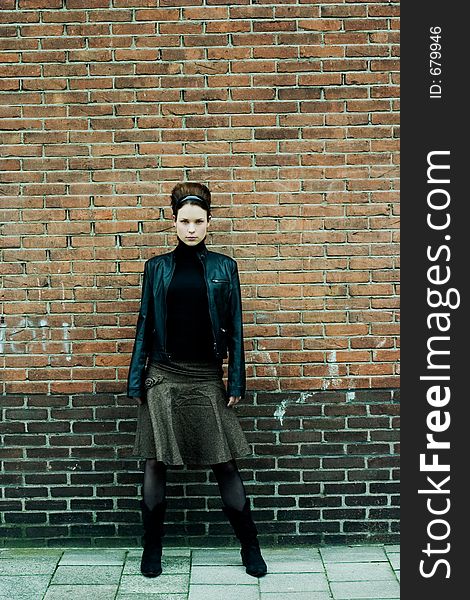 Fashionable model in skirt and leather jacket posing in front of a brick wall. Fashionable model in skirt and leather jacket posing in front of a brick wall