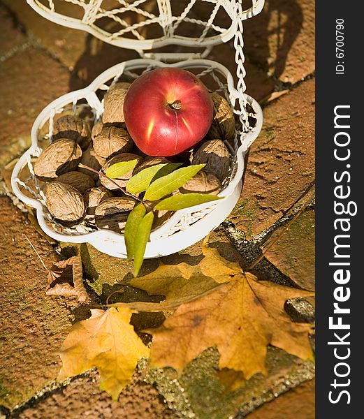 An apple and walnuts in an old white bascet