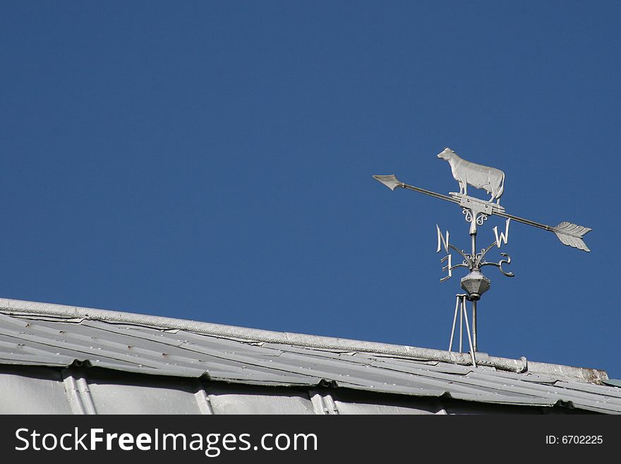 A cow weathervane on a barn roof, against a blue sky