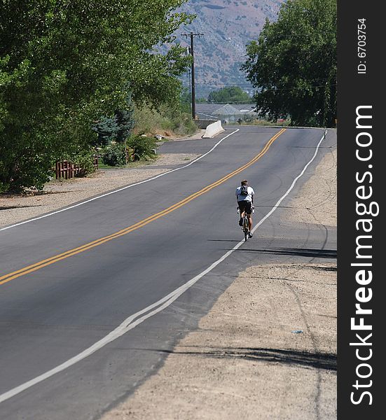 Solitary male riding bicycle on a rural road. Solitary male riding bicycle on a rural road.