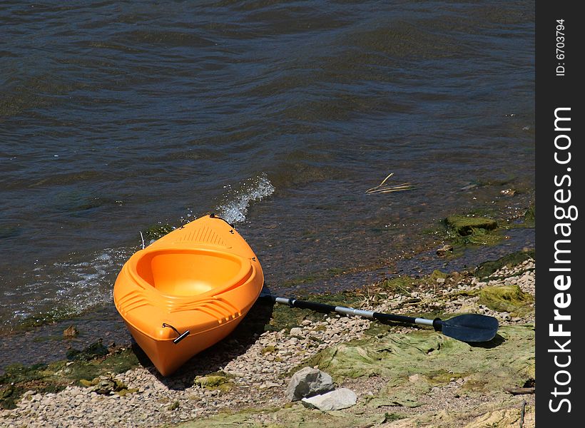 Orange kayak and paddle beached on lake shore