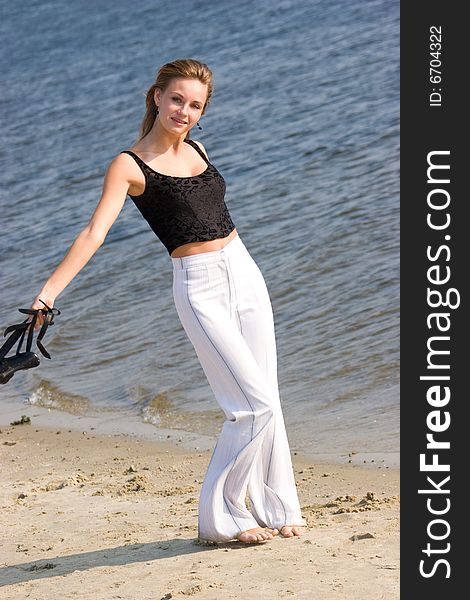 Beautiful woman in white slacks running on sea shore holding shoes