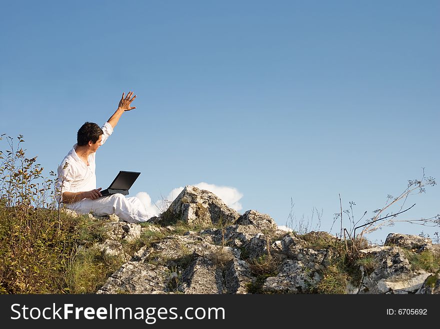 Young man using his laptop, sitting on the  rocky. Young man using his laptop, sitting on the  rocky